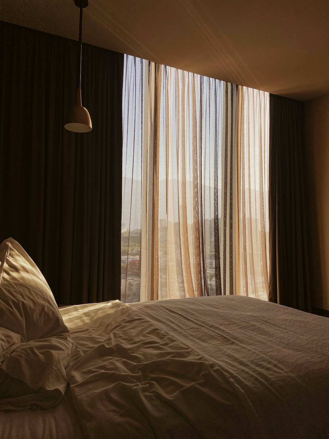 Camera da letto illuminata dal sole con letto sfatto e finestre con vista sulla città.